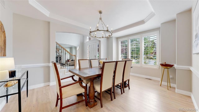 dining area with an inviting chandelier, a tray ceiling, and light hardwood / wood-style floors