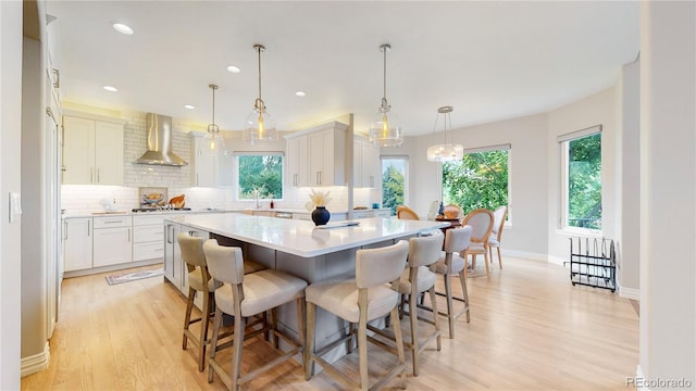 kitchen with a kitchen island, decorative light fixtures, white cabinets, light hardwood / wood-style floors, and wall chimney range hood