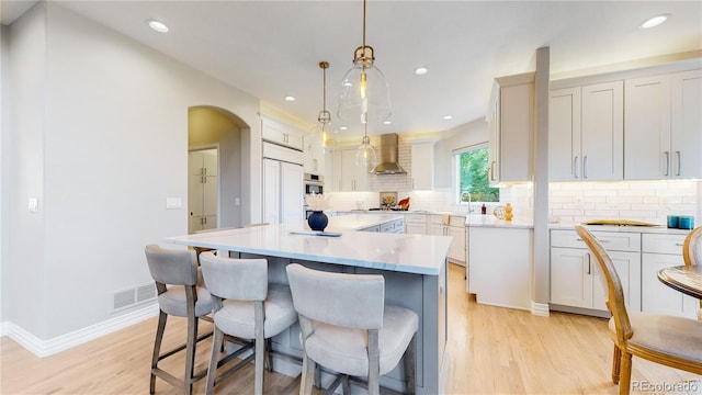 kitchen with decorative light fixtures, a center island, light wood-type flooring, decorative backsplash, and wall chimney range hood