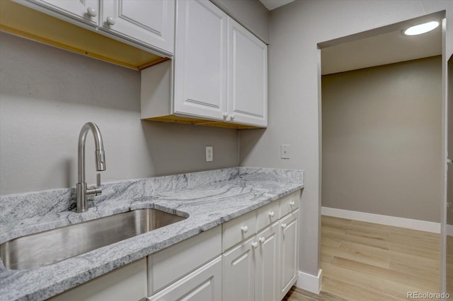 kitchen with baseboards, light stone countertops, light wood-type flooring, white cabinetry, and a sink