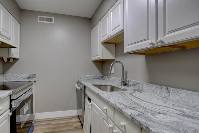 kitchen with under cabinet range hood, stainless steel appliances, a sink, visible vents, and light wood finished floors