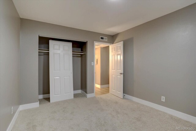 unfurnished bedroom with baseboards, visible vents, a closet, and light colored carpet