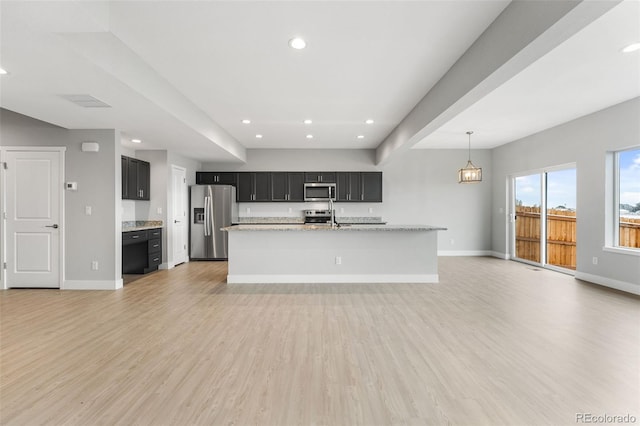 kitchen with light stone counters, stainless steel appliances, light wood-style flooring, open floor plan, and dark cabinetry