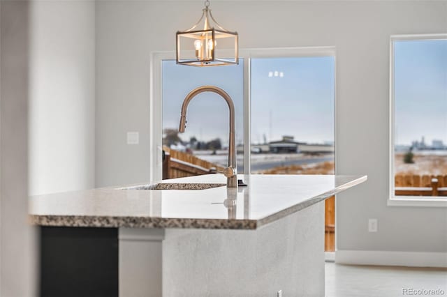 kitchen featuring light stone counters, decorative light fixtures, an inviting chandelier, a sink, and baseboards