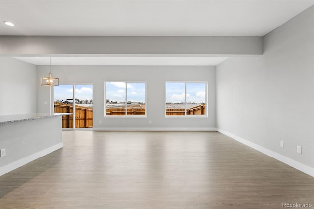 unfurnished living room featuring recessed lighting, an inviting chandelier, baseboards, and wood finished floors