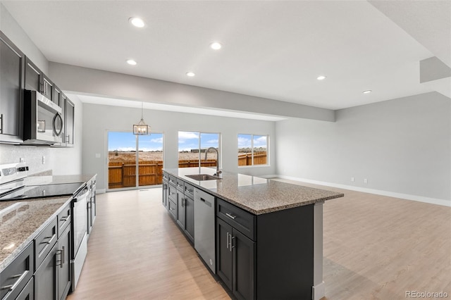 kitchen with a center island with sink, appliances with stainless steel finishes, light stone counters, and a sink