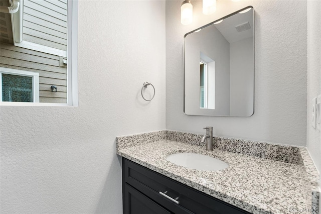 bathroom with a textured wall, visible vents, and vanity