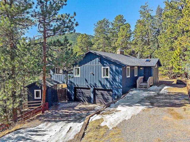 view of front of home with a view of trees, an attached garage, a chimney, and driveway