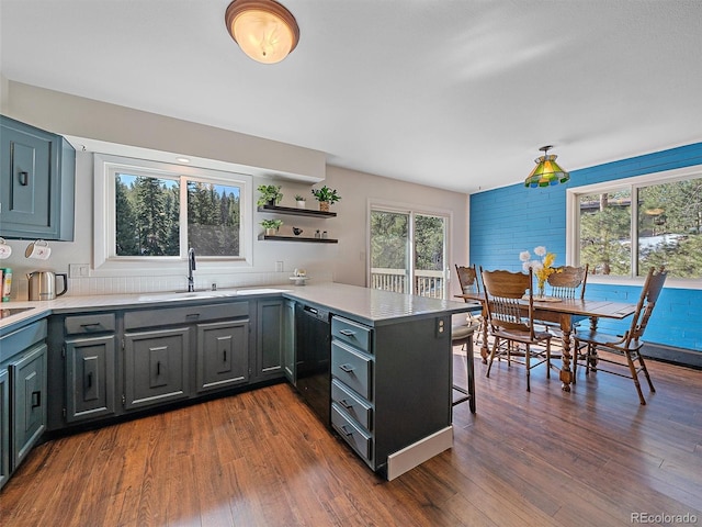 kitchen with a sink, dishwasher, a peninsula, a kitchen breakfast bar, and dark wood-style flooring