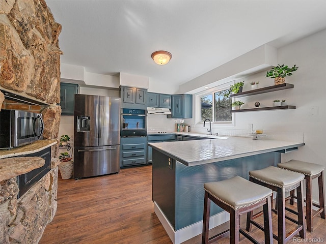 kitchen featuring under cabinet range hood, a kitchen bar, a peninsula, dark wood-style floors, and stainless steel appliances