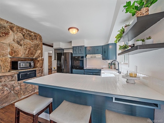 kitchen featuring blue cabinetry, oven, under cabinet range hood, fridge with ice dispenser, and a sink