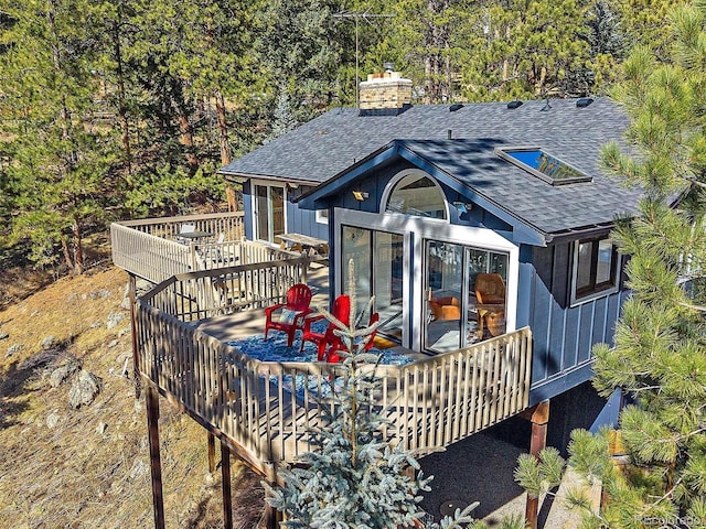 back of house featuring a chimney, a shingled roof, and a deck