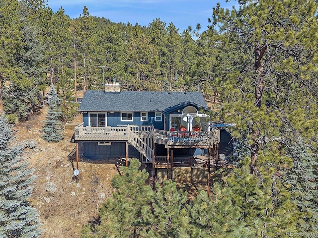 back of property with a wooden deck, a view of trees, a chimney, and stairway