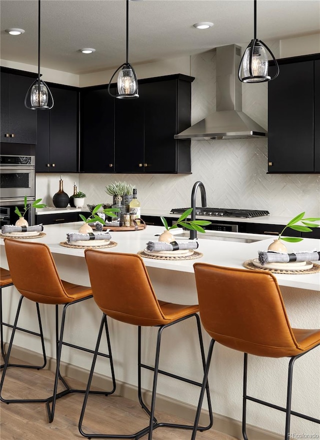 kitchen with pendant lighting, ventilation hood, light wood-type flooring, and stainless steel appliances