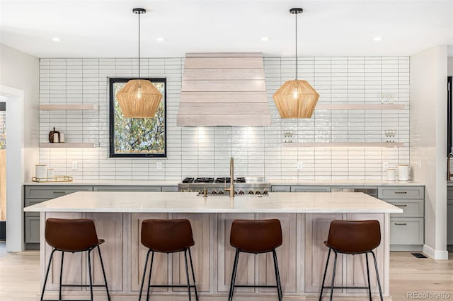 kitchen with light wood finished floors, open shelves, decorative backsplash, gray cabinetry, and premium range hood