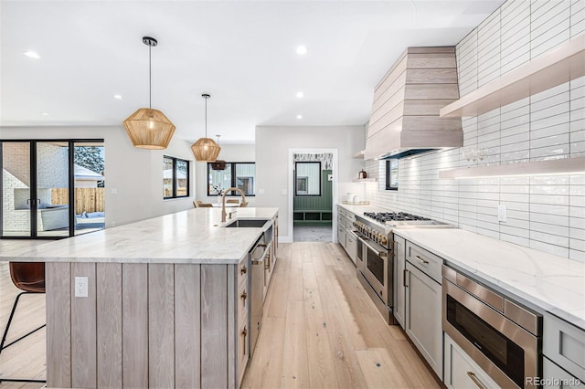 kitchen with light wood finished floors, tasteful backsplash, appliances with stainless steel finishes, gray cabinetry, and a sink