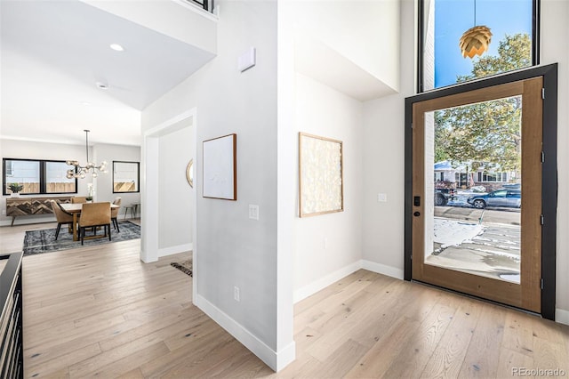 foyer entrance featuring a high ceiling, baseboards, light wood finished floors, and an inviting chandelier