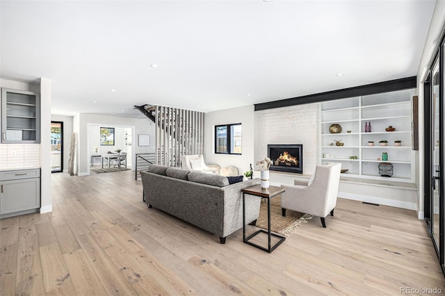 living area with a fireplace, recessed lighting, light wood-style flooring, stairway, and baseboards