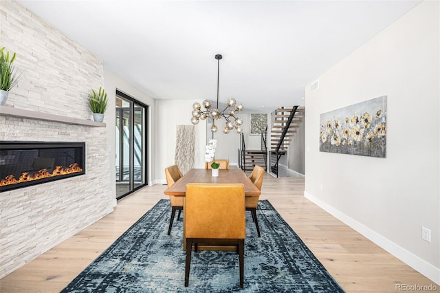 dining space with a chandelier, a stone fireplace, wood finished floors, baseboards, and stairs