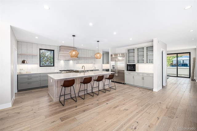 kitchen featuring built in fridge, a breakfast bar area, gray cabinets, light countertops, and light wood-style flooring