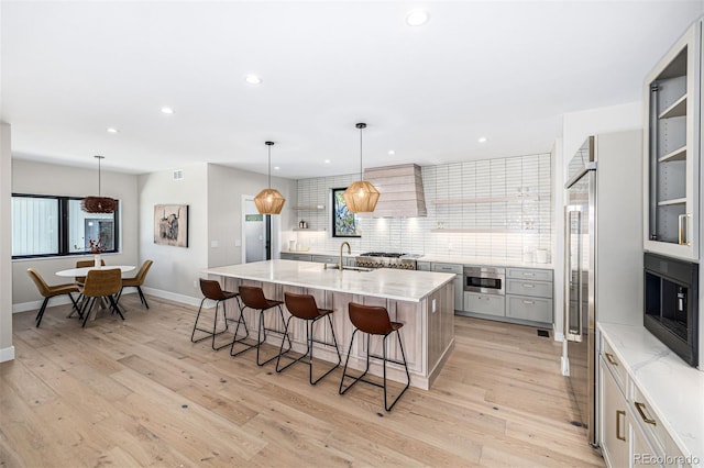 kitchen with light wood-style floors, custom range hood, appliances with stainless steel finishes, and a breakfast bar