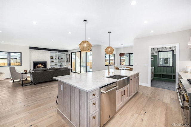 kitchen featuring a large fireplace, light wood finished floors, appliances with stainless steel finishes, a large island with sink, and a sink