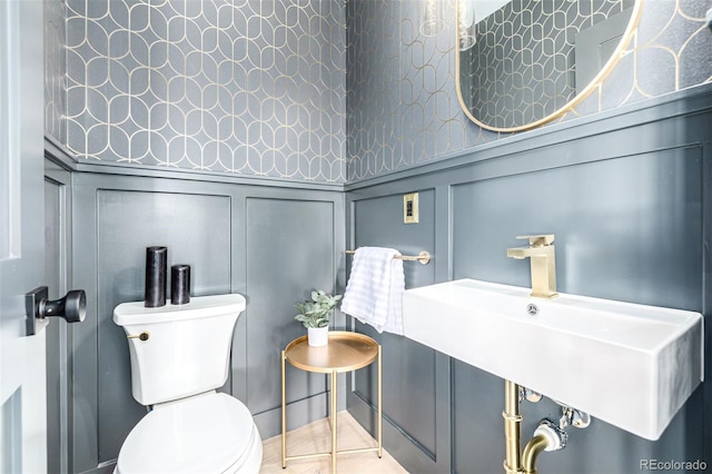 bathroom with tile patterned flooring, a sink, toilet, and a decorative wall