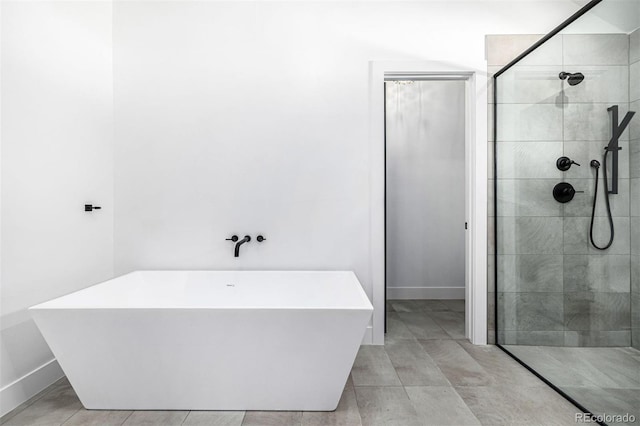 bathroom with a freestanding bath, a tile shower, and baseboards