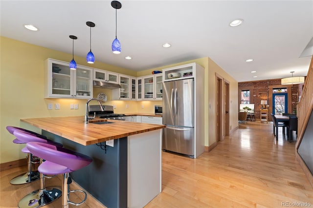 3313 Curtis St, Denver, CO 80205 - kitchen featuring butcher block countertops, stainless steel appliances, a peninsula, under cabinet range hood, and light wood-style flooring