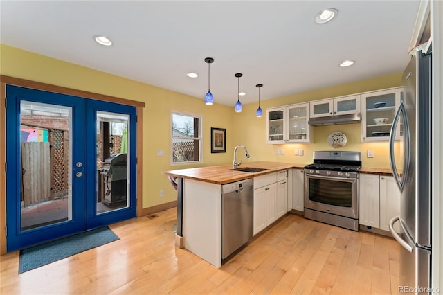 3313 Curtis St, Denver, CO 80205 - kitchen with appliances with stainless steel finishes, a peninsula, a sink, wood counters, and under cabinet range hood