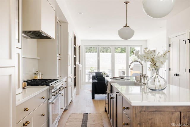 4131 Quivas St, Denver, CO 80211 - kitchen featuring stainless steel stove, premium range hood, a center island with sink, light wood-style floors, and light countertops