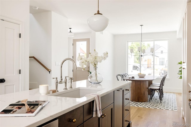 4131 Quivas St, Denver, CO 80211 - kitchen featuring light wood-type flooring, hanging light fixtures, dark brown cabinets, and light stone countertops