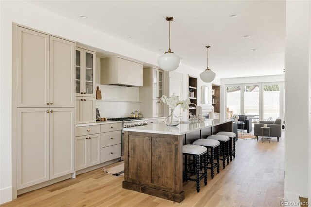 4131 Quivas St, Denver, CO 80211 - kitchen featuring stainless steel stove, light wood-style flooring, custom exhaust hood, an island with sink, and a breakfast bar