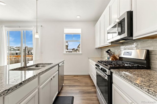 kitchen featuring light stone countertops, appliances with stainless steel finishes, sink, decorative light fixtures, and white cabinets