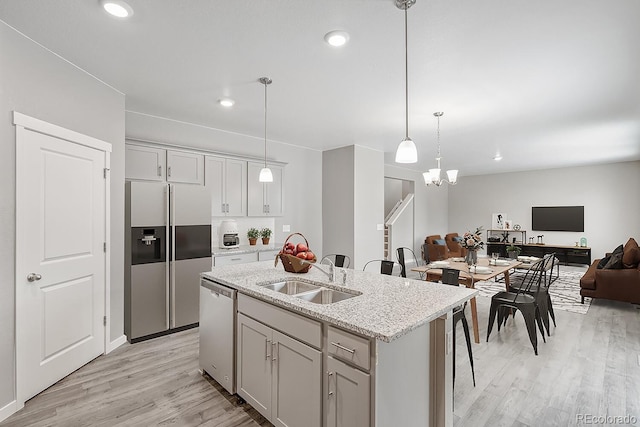 kitchen with light wood finished floors, a center island with sink, open floor plan, stainless steel appliances, and a sink