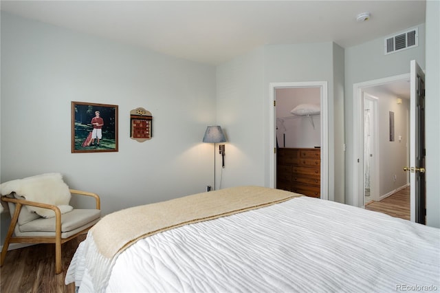 bedroom featuring a walk in closet, a closet, wood finished floors, and visible vents