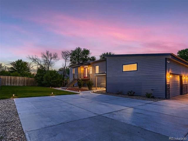 back of house at dusk with an attached garage, a lawn, fence, and driveway