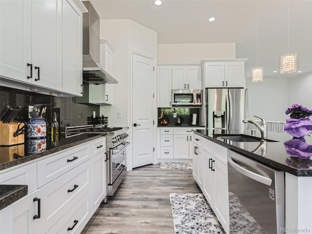 kitchen with wall chimney range hood, decorative backsplash, appliances with stainless steel finishes, white cabinetry, and a sink