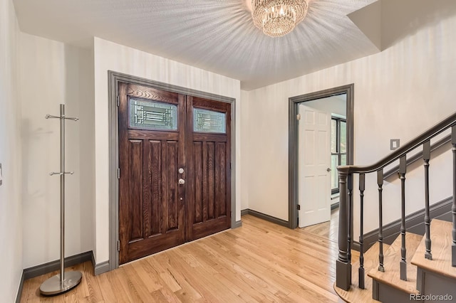 entrance foyer featuring baseboards, light wood finished floors, a chandelier, and stairway