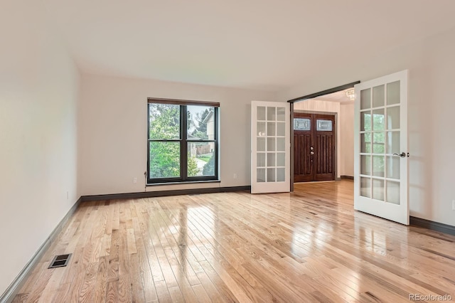 spare room featuring french doors, light wood-style flooring, and baseboards