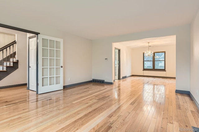 unfurnished room with a chandelier, light wood-style flooring, stairway, and baseboards