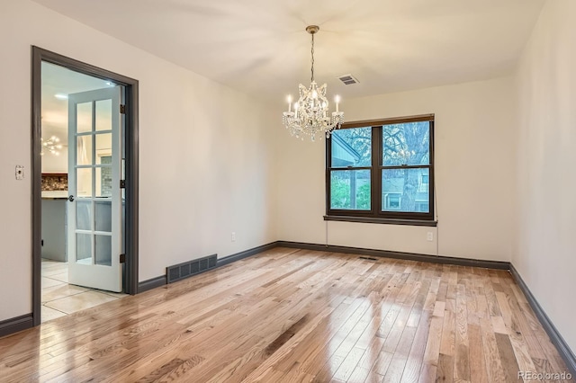 spare room with a chandelier, light wood finished floors, and baseboards