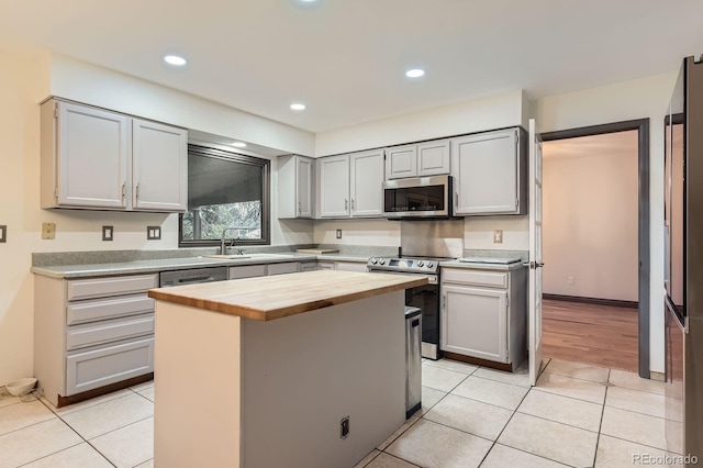 kitchen featuring butcher block counters, stainless steel appliances, a sink, light tile patterned flooring, and gray cabinetry