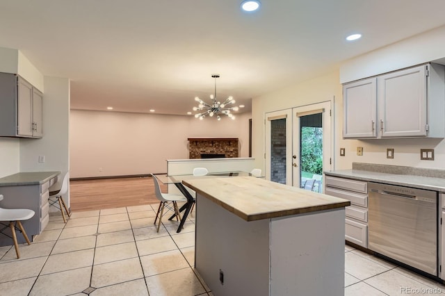 kitchen featuring stainless steel dishwasher, butcher block countertops, gray cabinetry, light tile patterned floors, and a chandelier