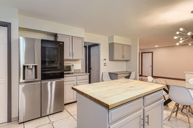 kitchen with stainless steel fridge, butcher block counters, light tile patterned floors, gray cabinets, and a chandelier