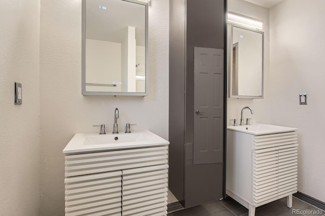 bathroom with two vanities, a textured wall, and tile patterned floors
