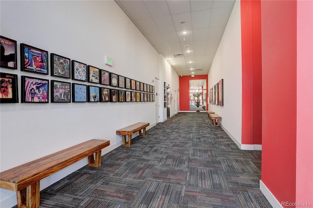 hallway featuring a paneled ceiling, carpet flooring, and baseboards