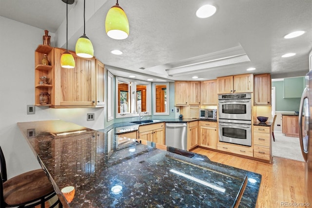 kitchen featuring kitchen peninsula, sink, pendant lighting, light wood-type flooring, and appliances with stainless steel finishes