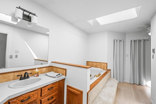 bathroom with wood-type flooring, a skylight, ceiling fan, a bathing tub, and vanity