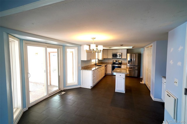 kitchen featuring light stone countertops, hanging light fixtures, a kitchen island, white cabinets, and appliances with stainless steel finishes